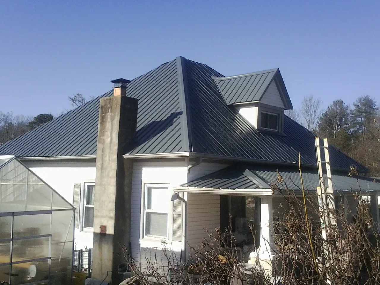 Dark blue standing seam metal roof on a white farmhouse with dormer — Slate & Tile Roof Repair by Roofing Brothers in Brantingham