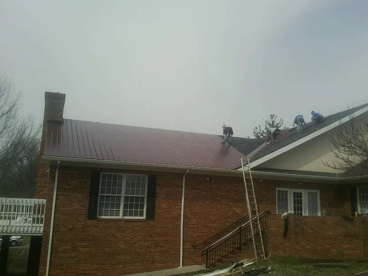 Crew setting red metal roofing panels on a brick home in Brantingham