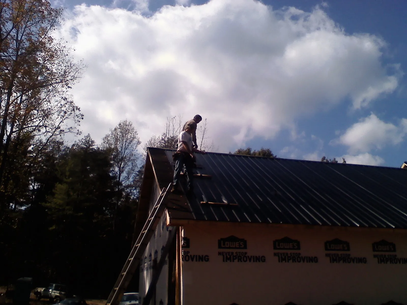 Roofer fastening dark metal panels high against a cloudy sky, from a Roof Inspection job in Brantingham