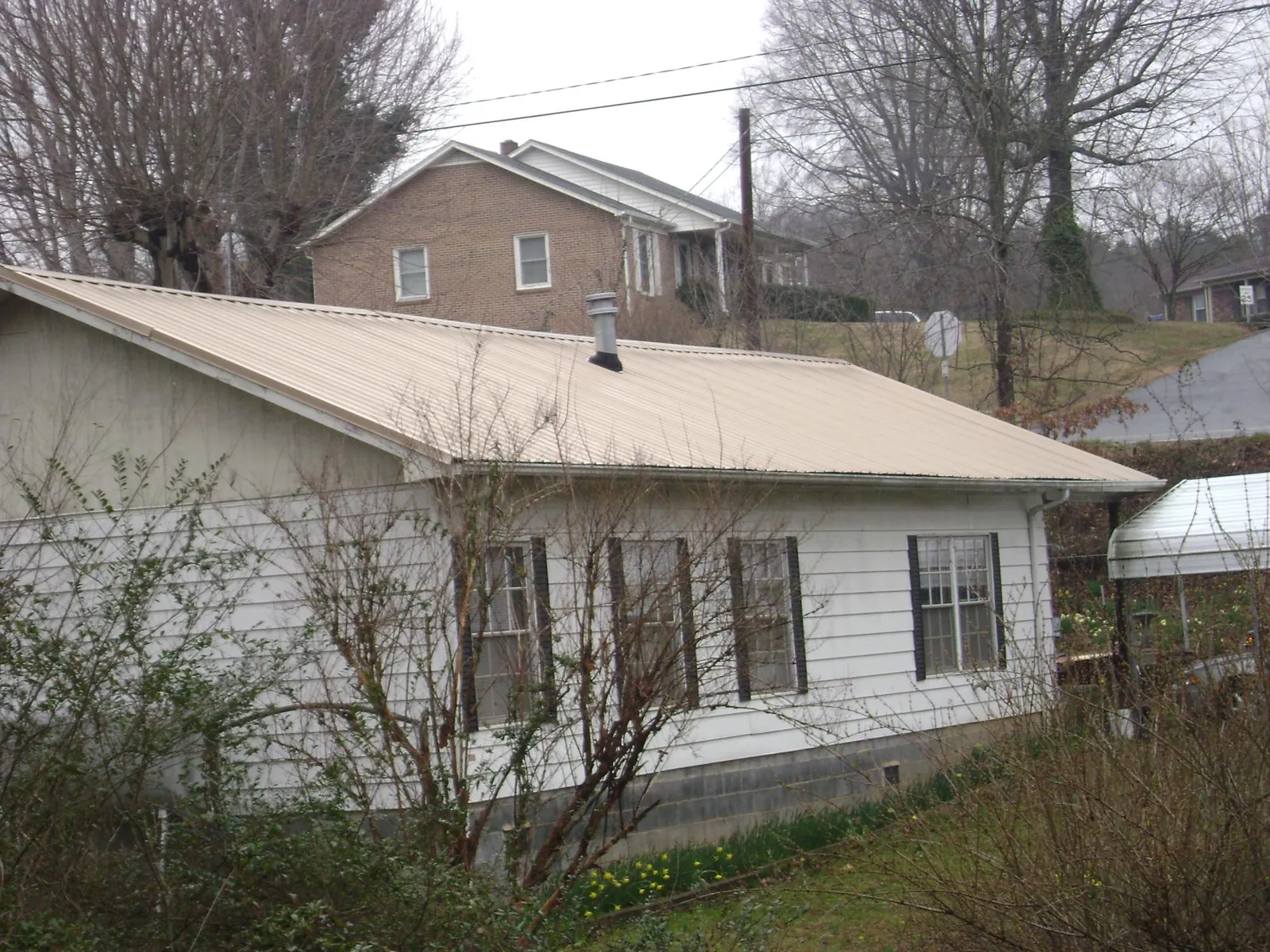 Tan metal roof on a white sided house set into a hillside — Commercial Roofing by Roofing Brothers in Brantingham