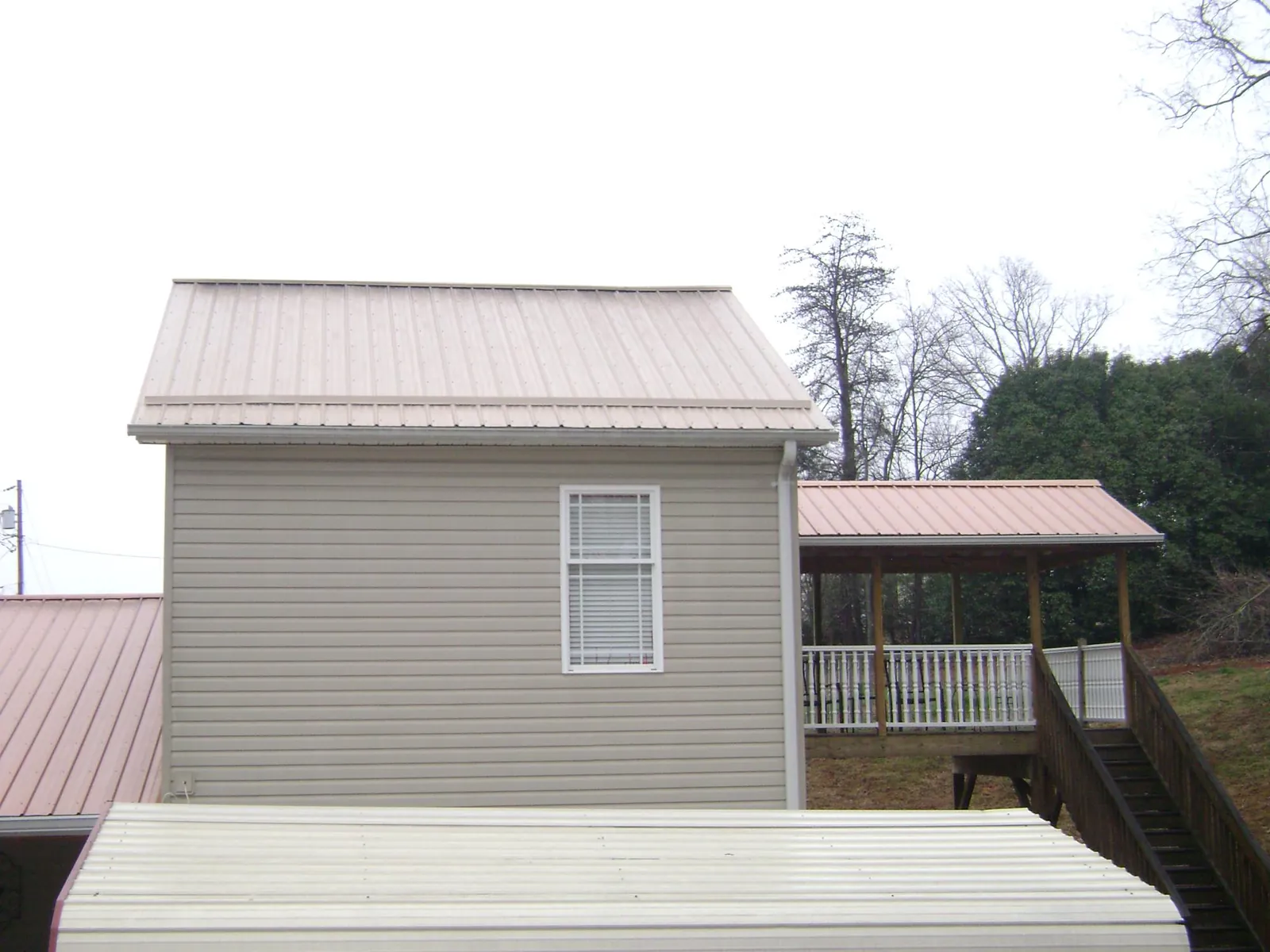 Tan metal roofs on a two story addition and attached porch, from a Roof Replacement job in Brantingham